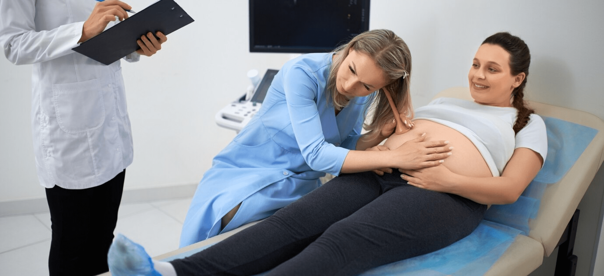 Obstetrician and gynecologist examining a pregnant woman lying in a hospital bed.